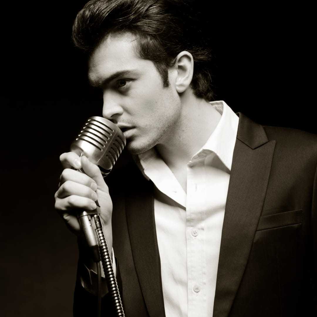 Male singer in suit passionately performing with vintage microphone.