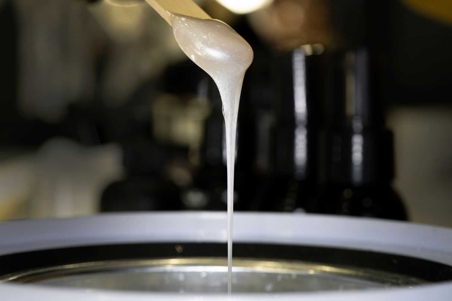 Hot wax dripping from stick into pot, ready for hair removal treatment.