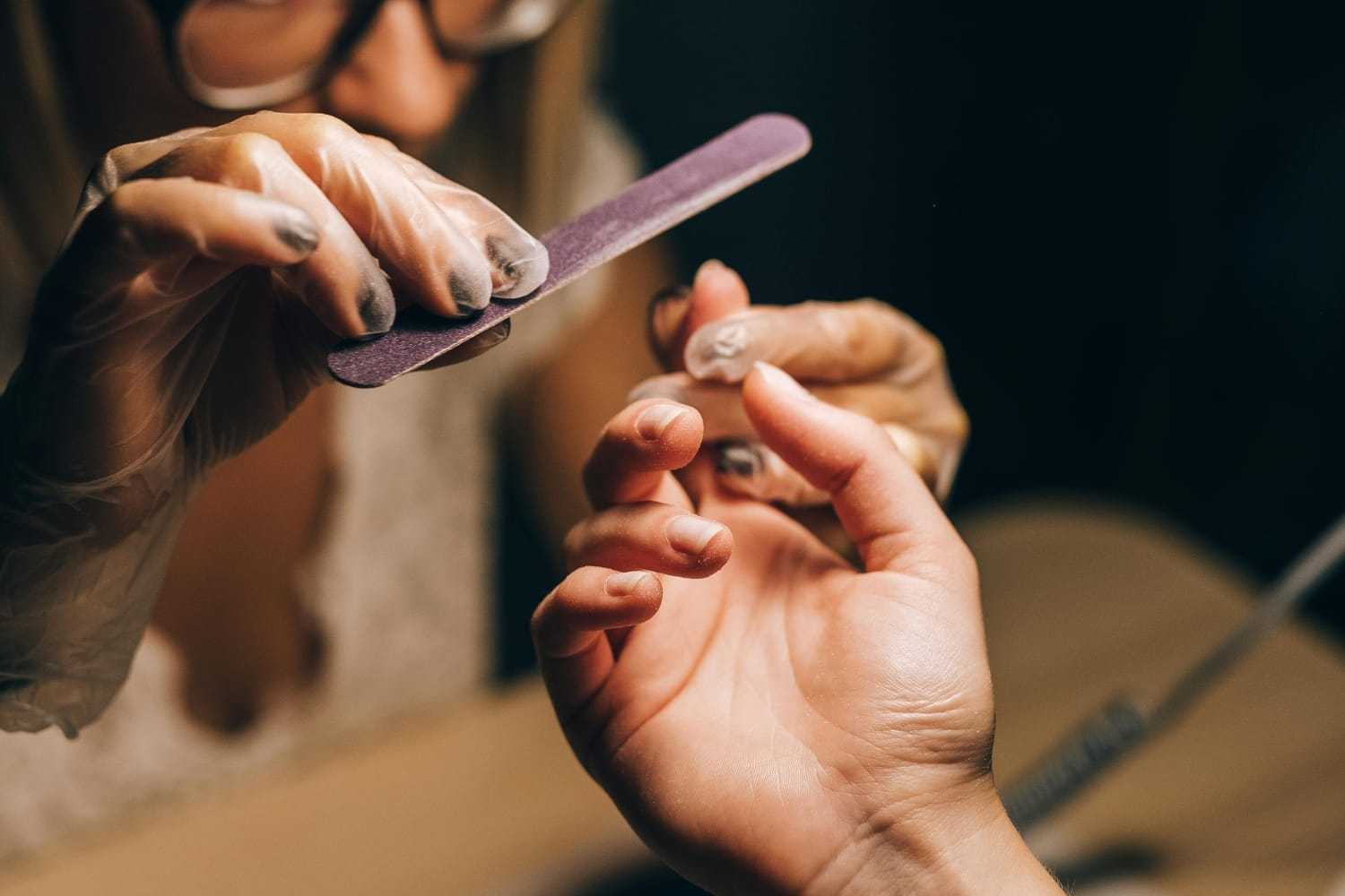 Manicure in progress: gloved hands filing client's nails at a salon.