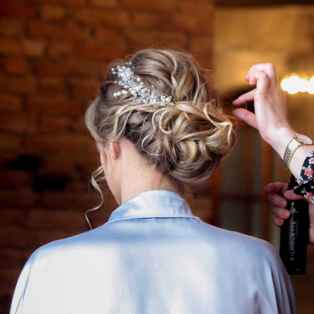Woman with styled updo being adjusted by hairstylist, wearing a blue satin robe.